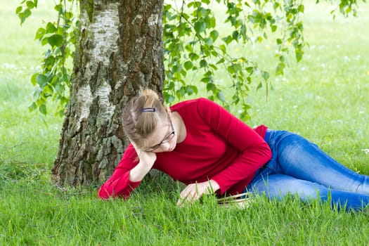 Young girl reading book in park in spring day