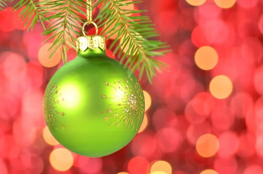 christmas decoration, green Christmas ball hanging on spruce twig against bokeh background
