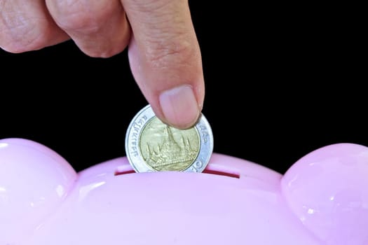Hand inserting coin into piggy bank