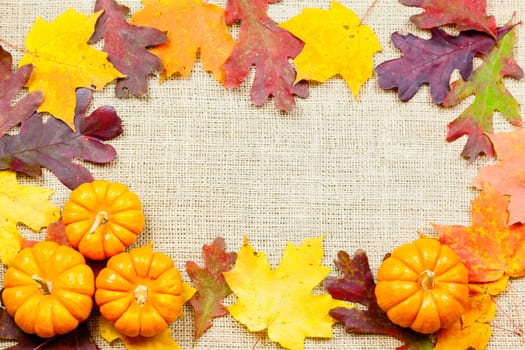 Fall-themed background of burlap, dry leaves and pumpkins