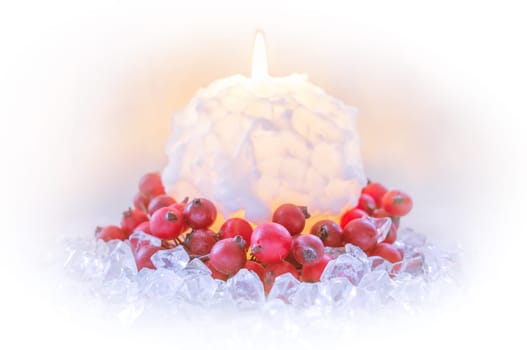 Christmas candle in the shape of a snowball surrounded by red berries on ice