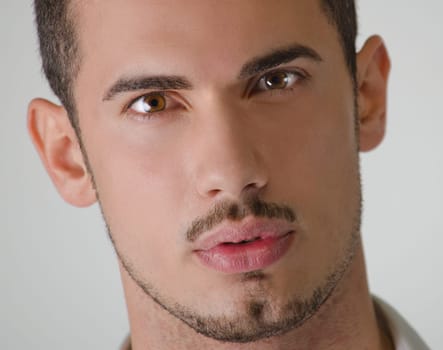 Head shot of attractive young man looking at camera with piercing brown eyes, on light background