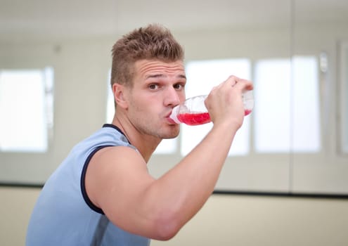 Attractive, nice male athlete drinking red beverage from plastic bottle