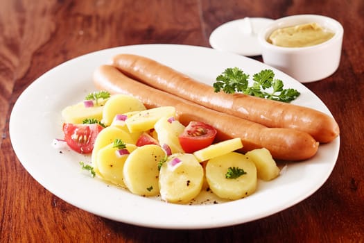 Two smoked frankfurters served with boiled baby potatoes and tomato with an accompaniment of mustard