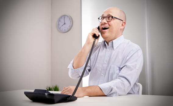 Man in an office listening to a phone, smiling and looking upleft