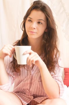 Young girl with long brunette hair in pajamas is lounging in her four-poster bed on Sunday morning.