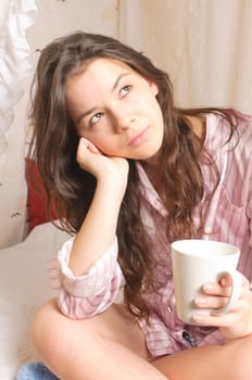 Young girl with long brunette hair in pajamas is lounging in her four-poster bed on Sunday morning.