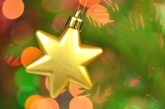 christmas decoration, golden Christmas star ball hanging on spruce twig against bokeh background