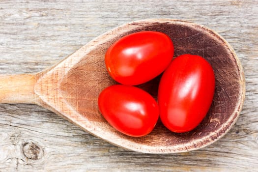 Spoon with small tomatoes on a wooden background