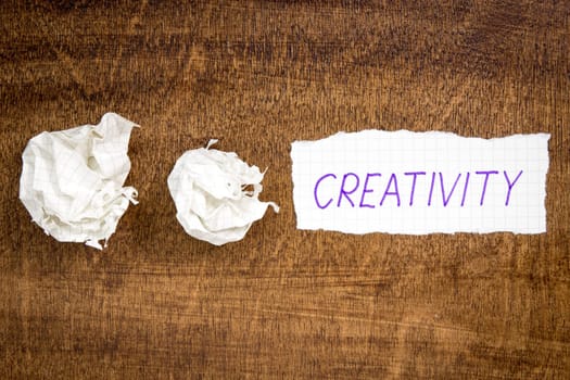 Sheet of paper with word CREATIVITY and crumpled wads on table