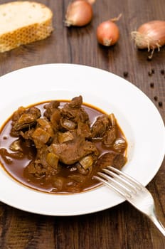 Fork and plate with wild goulash on a wooden table