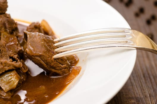 Close-up of goulash on a fork above a plate