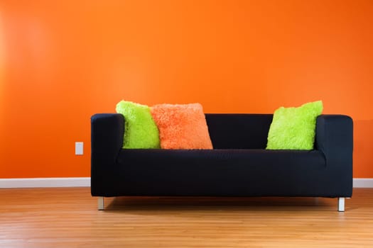 Contemporary black couch against bright orange wall in a modern living room