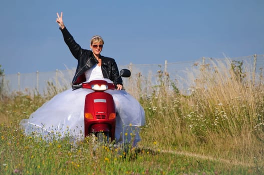 Bride in white wedding dress rides on a moped to the wedding ceremony