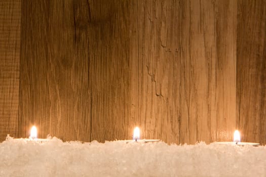 several candles in the snow with wooden background