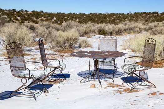 Four empty garden chairs around a table in the desert with snow