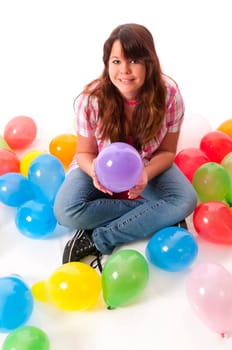 Teenage girl sits on the floor and stretches her hands up to catch colorful balloons against a white background