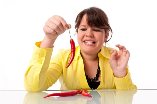 Teenage girl with long hair and yellow blouse is afraid of a hot chili pepper against a white background.
