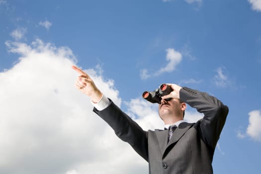 Businessman is looking ahead through binoculars with sky in the background