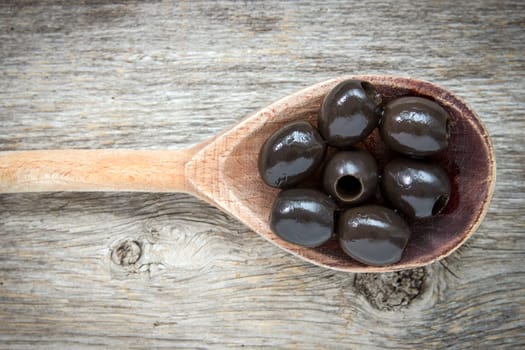 Spoon with black olives on a wooden background