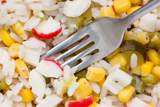 Fork in a salad with fresh vegetables and crab sticks