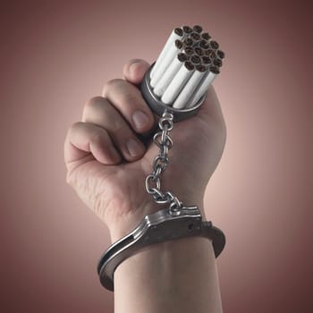 Cigarettes stuck on hand by a handcuff, concept of addiction.