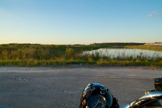 Looking over the handlebars of a vintage motorcycle at the end of the road that leads to a swampland pond in rural florida.
