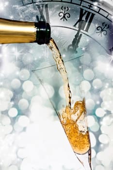 Pouring champagne against holiday lights and clock close to midnight