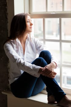 Attractive young woman sitting on the window sill