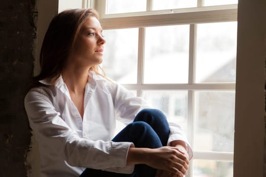Attractive young woman sitting on the window sill