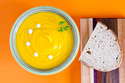 Pumpkin soup in a bowl with bread on orange placemat