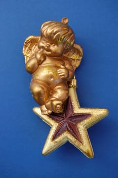Little angel sitting on golden christmas star bauble. Seasonal decoration.