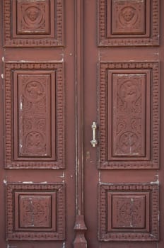 Wooden church door with carved religious symbols. Angels and cross motif.
