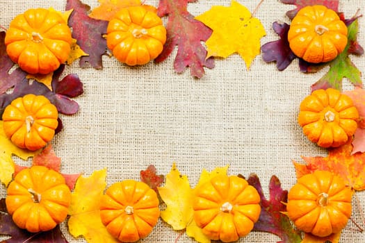 Fall-themed background of burlap, dry leaves and pumpkins