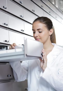 Young woman pharmacist taking medicine from drawer
