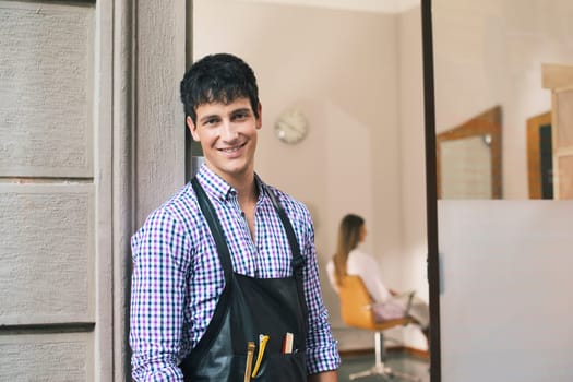 portrait of young male hairstylist standing out of shop and looking at camera
