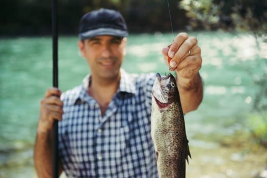 mid adult fisherman on holidays on river, relaxing and fishing trout. Focus on fish
