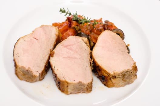 Pink roasted pork tenderloin on steamed tomatoes and olives