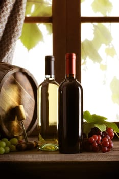 Wine bottles with grapes and barrel on old wooden table