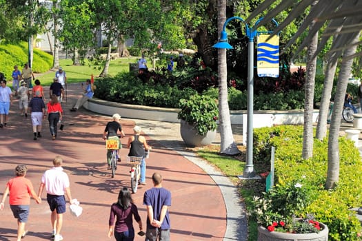FORT LAUDERDALE, FLORIDA - FEBRUARY 3, 2013: Lots of people enjoying walking and biking on the brick walkway that travels along beautiful Riverwalk park in downtown on a sunny and warm winter day.