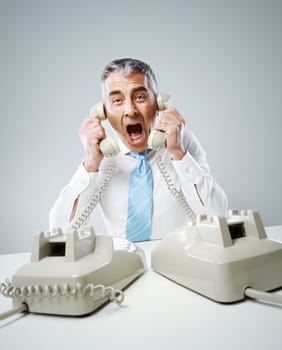 A stressed businessman shouts into the two handsets that he is holding.