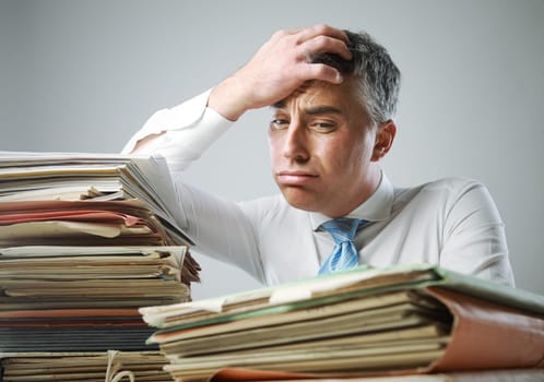 Stressed businessman, with a too much paperwork and files piled up on the table