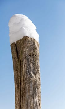 Wooden pole with snow against a blue sky