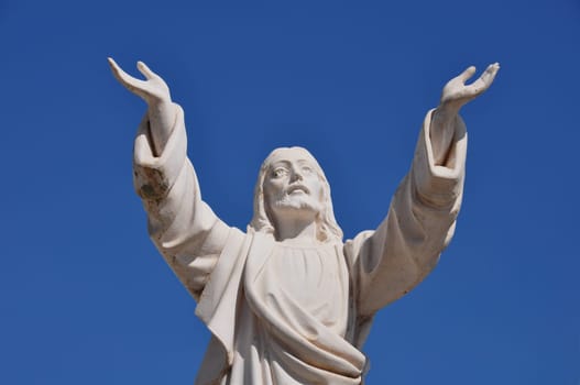 Jesus Christ with hands raised in blessing under blue sky. Marble funerary statue.