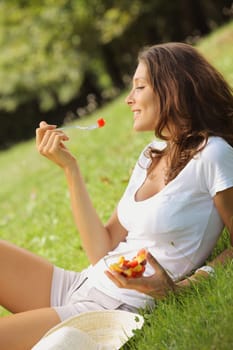 Beautiful woman eating fruit salad on a lawn