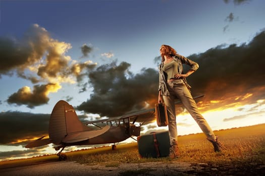 Fashion young womanl with a suitcase. Airplane in the background.