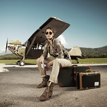 Beautiful young woman sitting on a suitcase at the airport. Airplane in the background