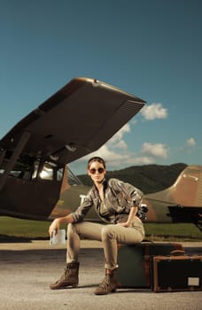 Beautiful young woman sitting on a suitcase at the airport. Airplane in the background
