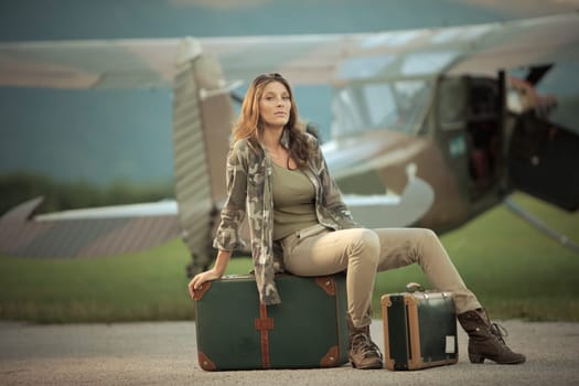 Beautiful young woman sitting on a suitcase at the airport. Airplane in the background