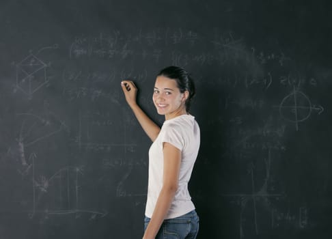 A young female student is standing in front of the blackboard going to draw something with a chalk.